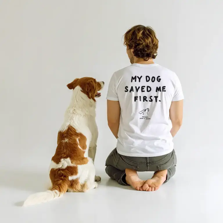 Mann sitzt auf dem Boden von hinten, trägt ein weißes T-Shirt aus Bio-Baumwolle mit schwarzem Tierschutz-Spruch ‚Adopt, Don’t Shop‘, Hund sitzt neben ihm