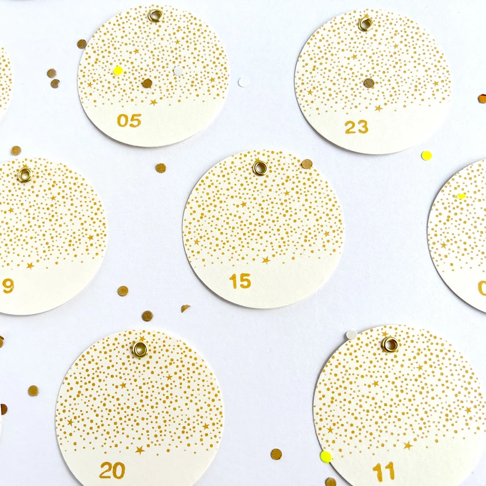 24 runde Adventskalender-Zahlenanhänger aus Naturpapier mit goldfarbenen Metallösen im funkelnden Stempel-Design, ideal zum Basteln von DIY Adventskalendern, um Freunde, Familie oder Partner zu überraschen